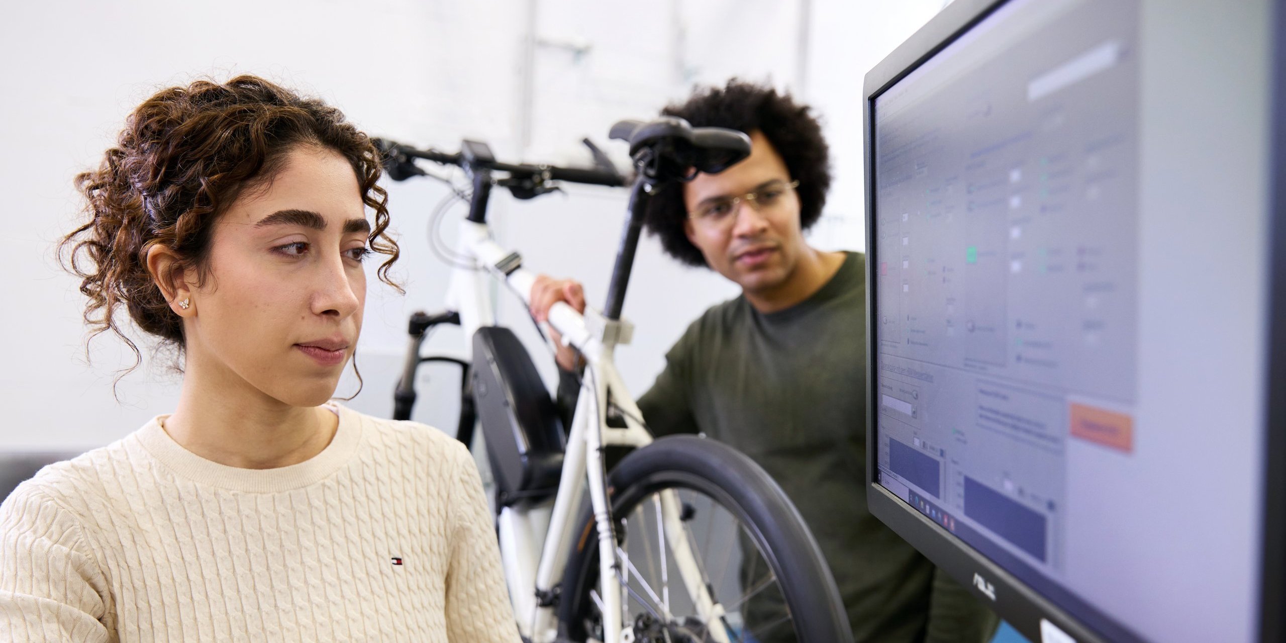 Person in foreground looking at screen, person in background on e-bike