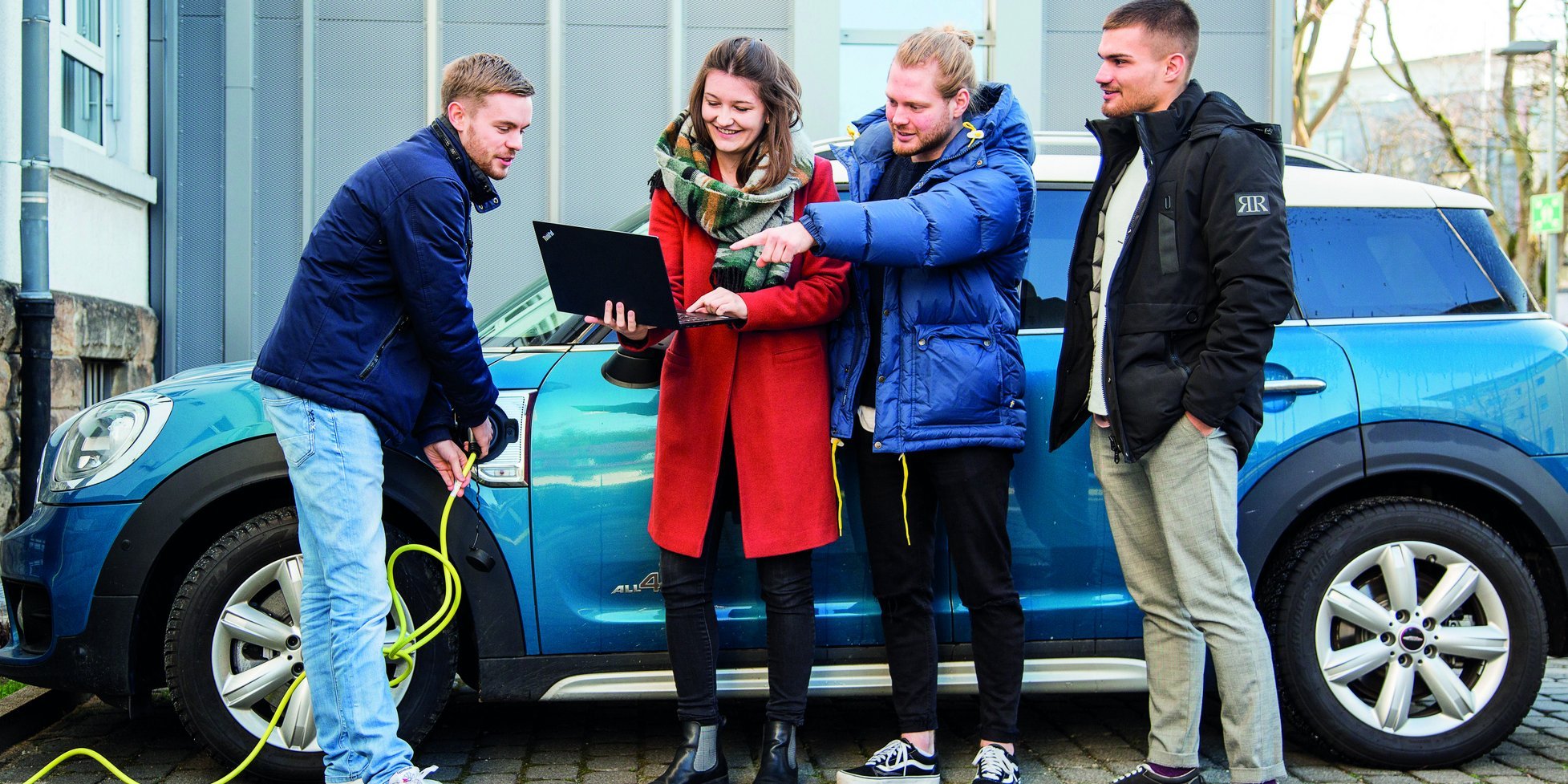 Four people with notebook in front of an electric car