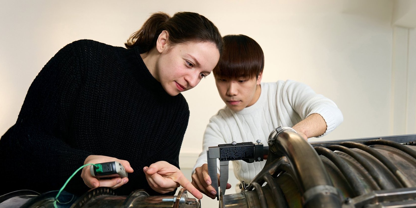 Two people with measuring devices on a machine part