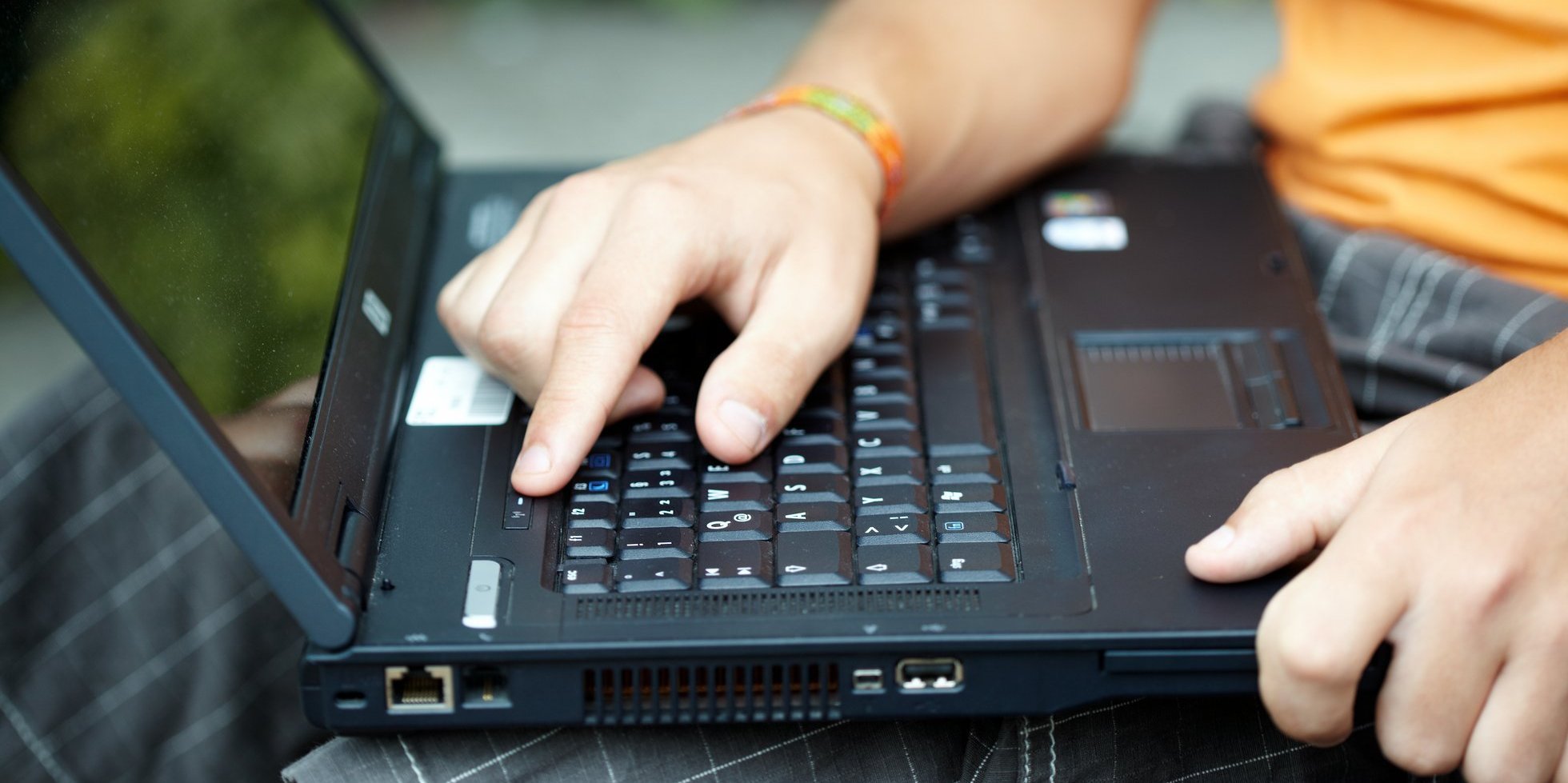 Ein Student hat ein Laptop auf dem Schoß. Auf dem Bild sieht man, wie der Student auf einen Knopf auf dem Laptop drückt.