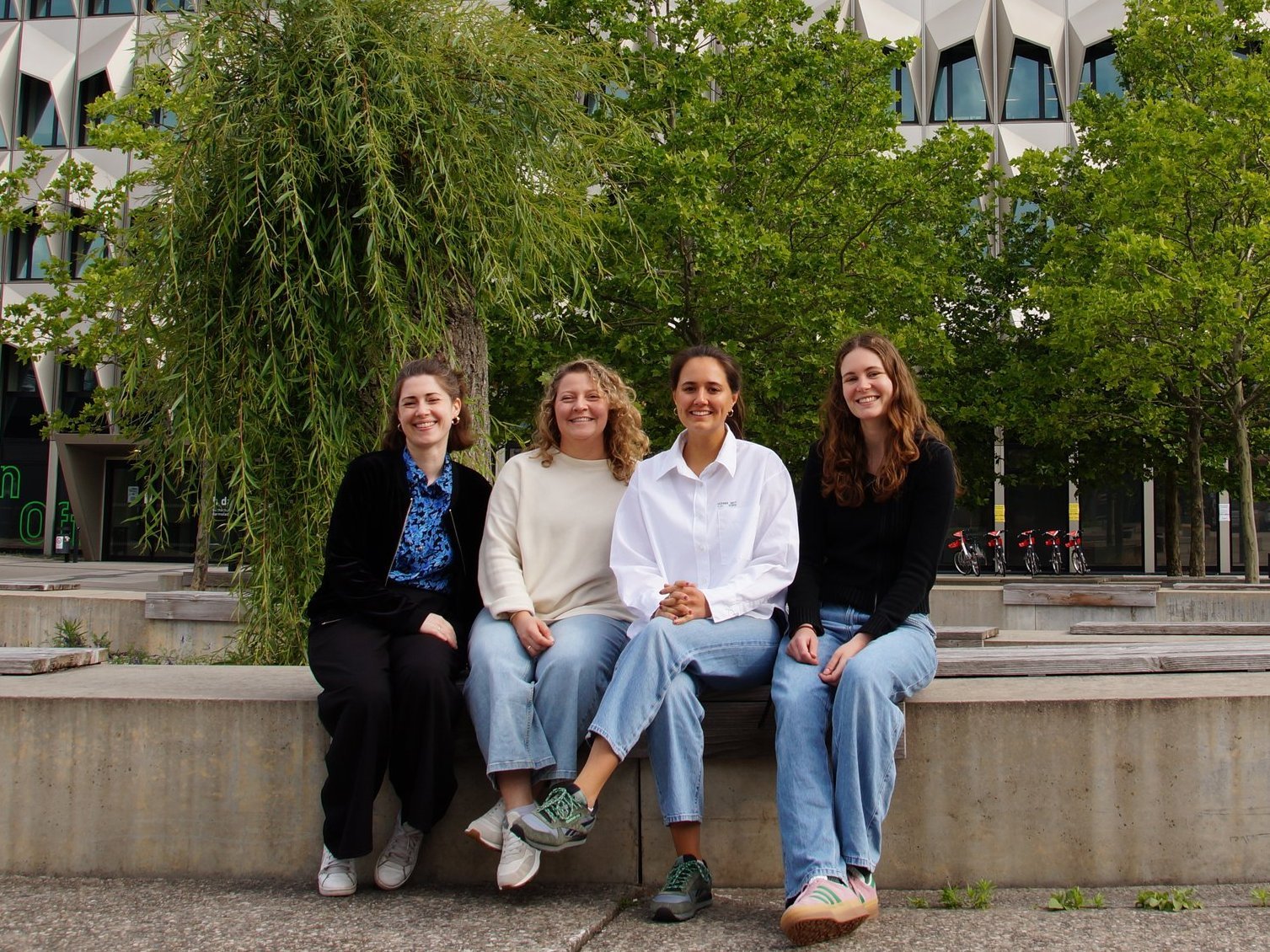Vier Personen sitzen vor dem Hochhaus der Hochschule Darmstadt.