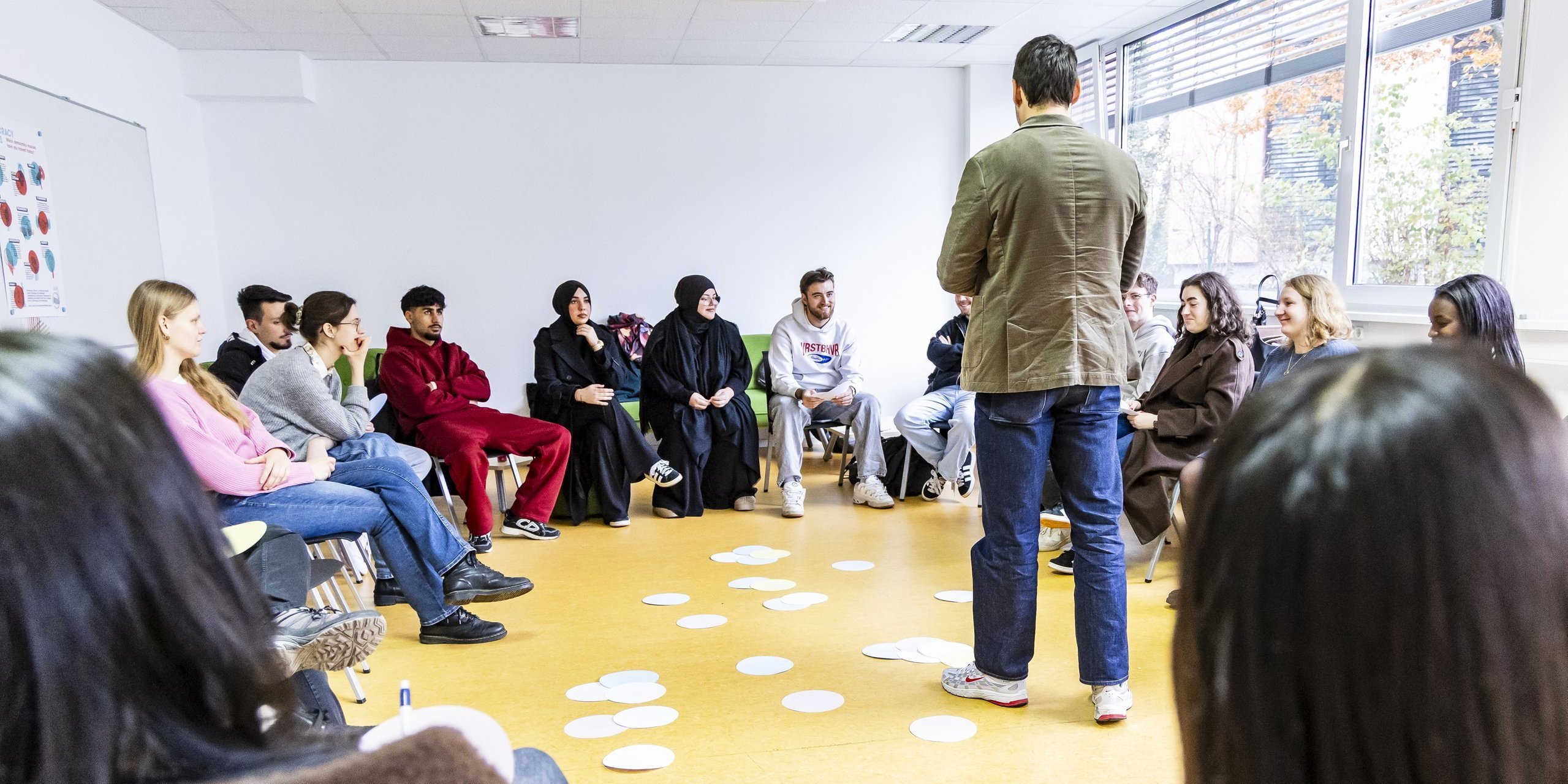 Ein Workshop-Teilnehmer steht inmitten der anderen sitzenden Teilnehmer:innen und erklärt etwas