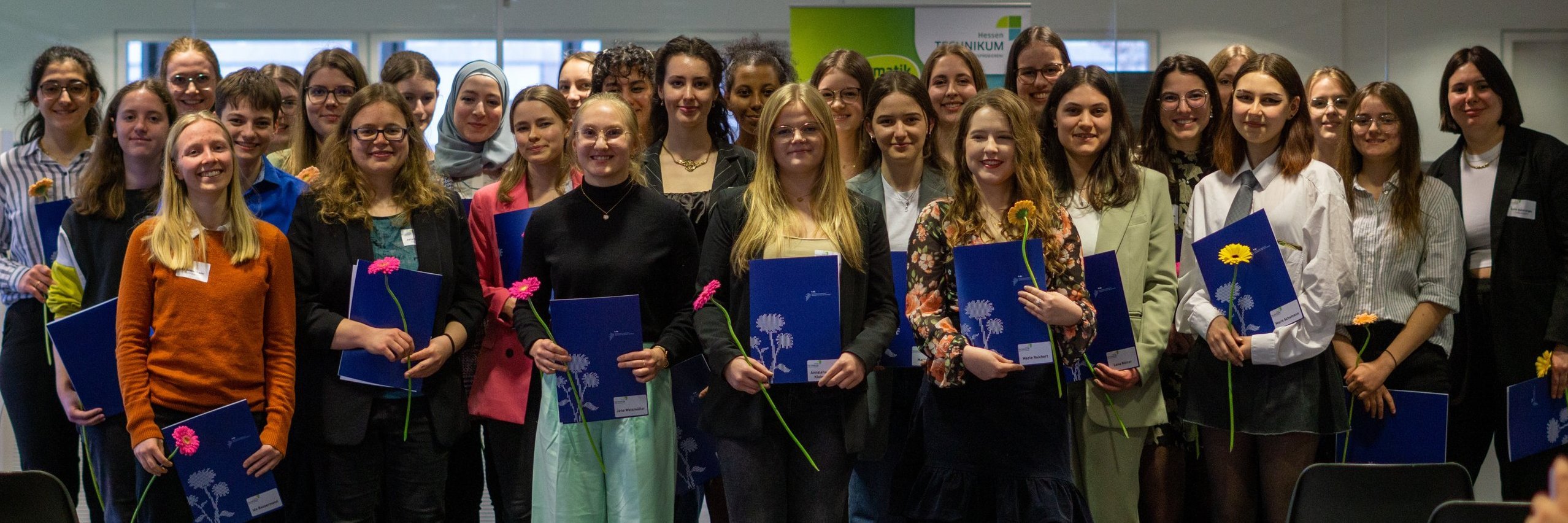 Abschlussbild der Teilnehmerinnen des Hessen-Technikums. 35 junge Frauen, stehen mit Zertifikaten und einer rose Blume in drei Reinen und lächen. 