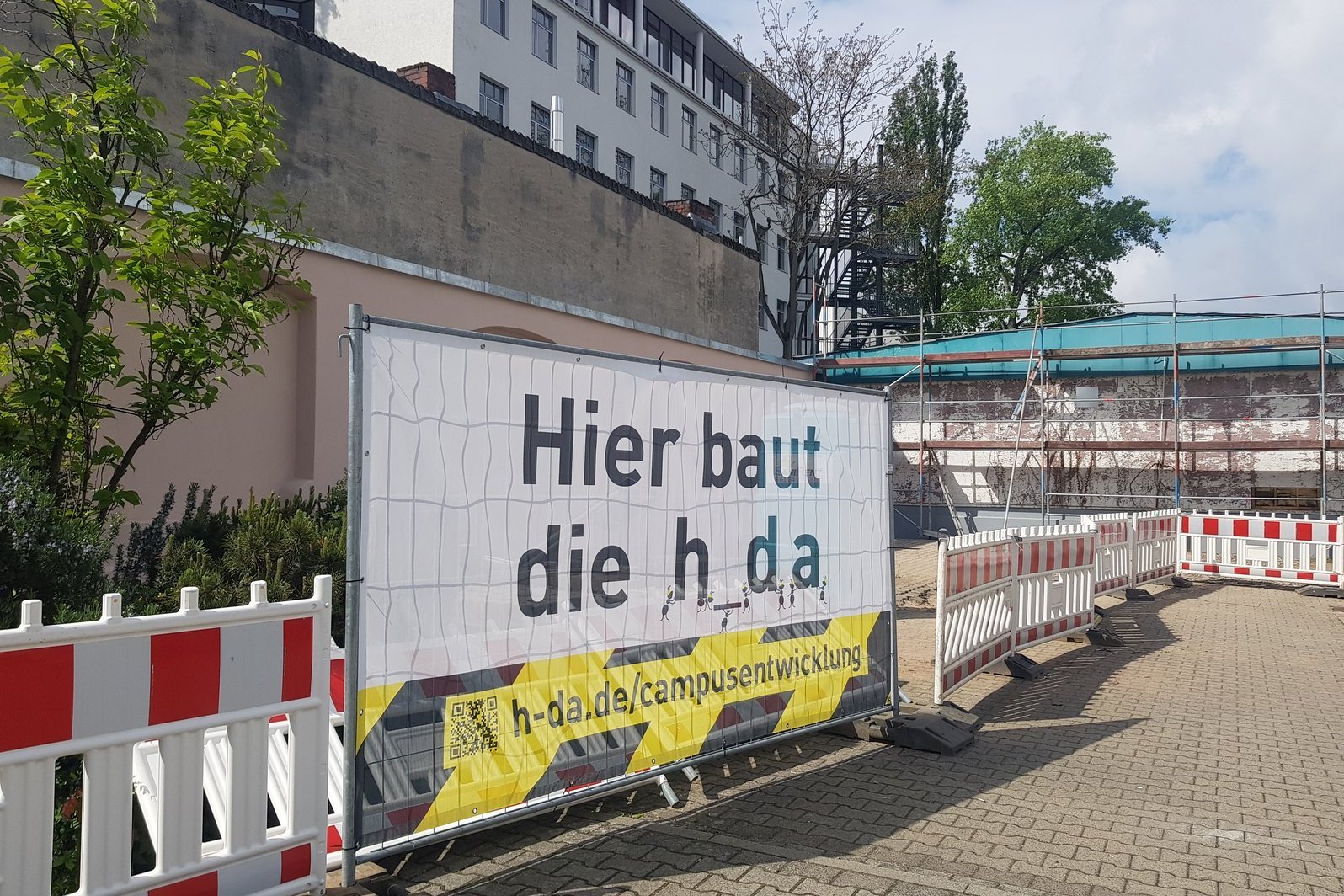 Blick auf das Banner am Bauzaun mit schwarz-gelber Grafik "Hier baut die h_da"