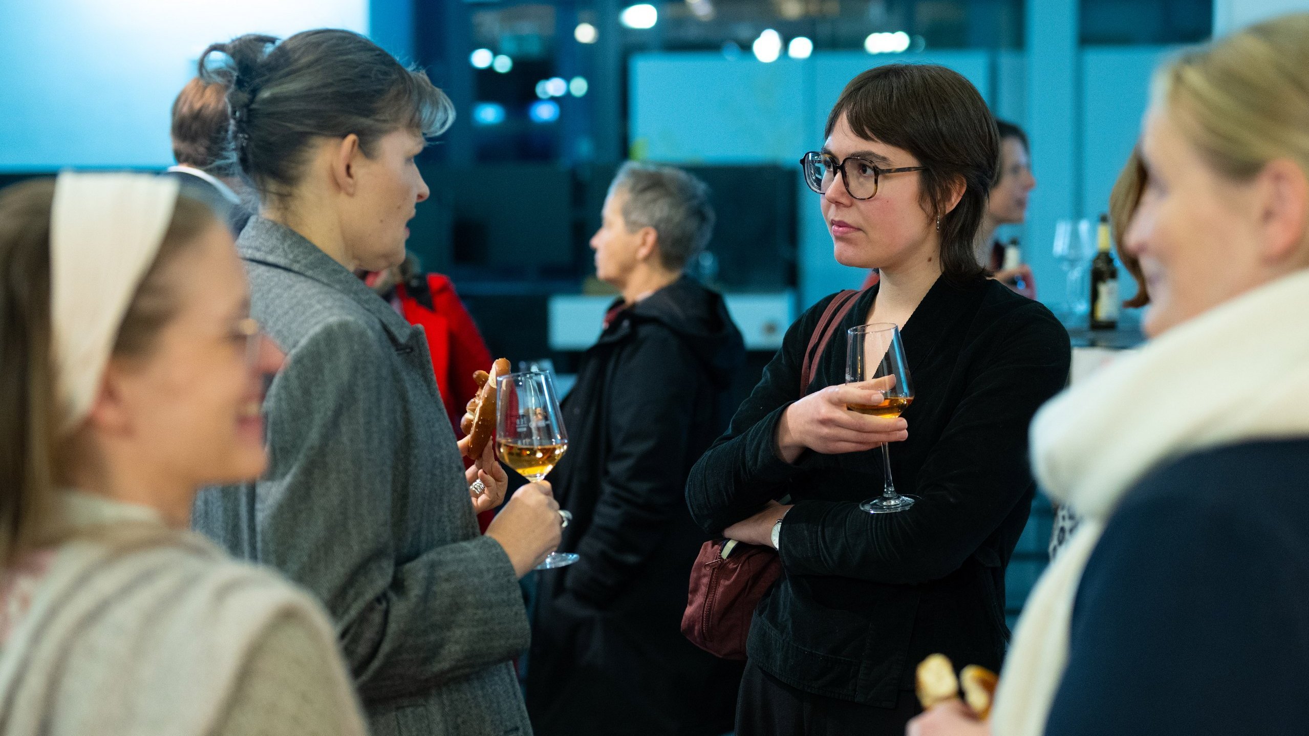 Panelisten und Gäste stehen bei Brezeln und Wein zusammen