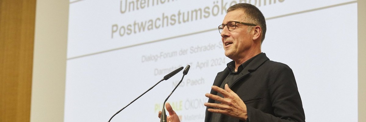 Das Foto zeigt Prof. Dr. Nico Paech, der gestikulierend spricht. Im Hintergrund ist seine Präsentation zu sehen, auf der das Wort Postwachstumsökonomie zu lesen ist.