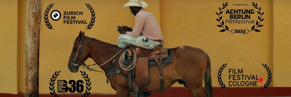 Das Foto zeigt einen Cowboy, der auf einem Pferd sitzend mit einem Mobiltelefon beschäftigt ist. An einer im Saloon-Stil gestalteten Wand im Hintergrund sind Schriftzüge zu sehen: ZURICH FILM FESTIVAL, ACHTUNG BERLIN Filmfestival, B36 und FILM FESTIVAL COLOGNE.