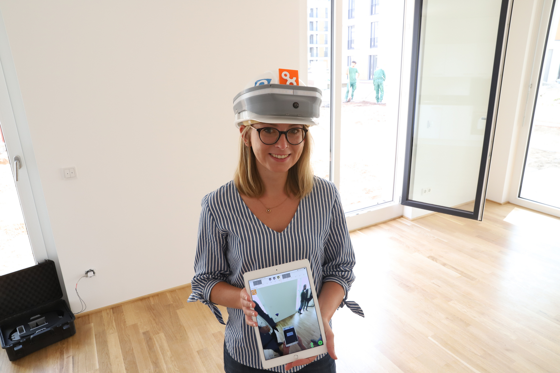 Eine Frau hält auf einer Baustelle ein Tablet in der Hand und trägt einen speziellen Helm.