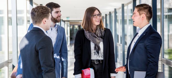 Four people in business attire have a standing conversation in a hallway